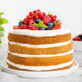 Homemade naked layered vanilla cake with whipped cream and fresh berries on top on a gray concrete background. Summer cake. Copy space